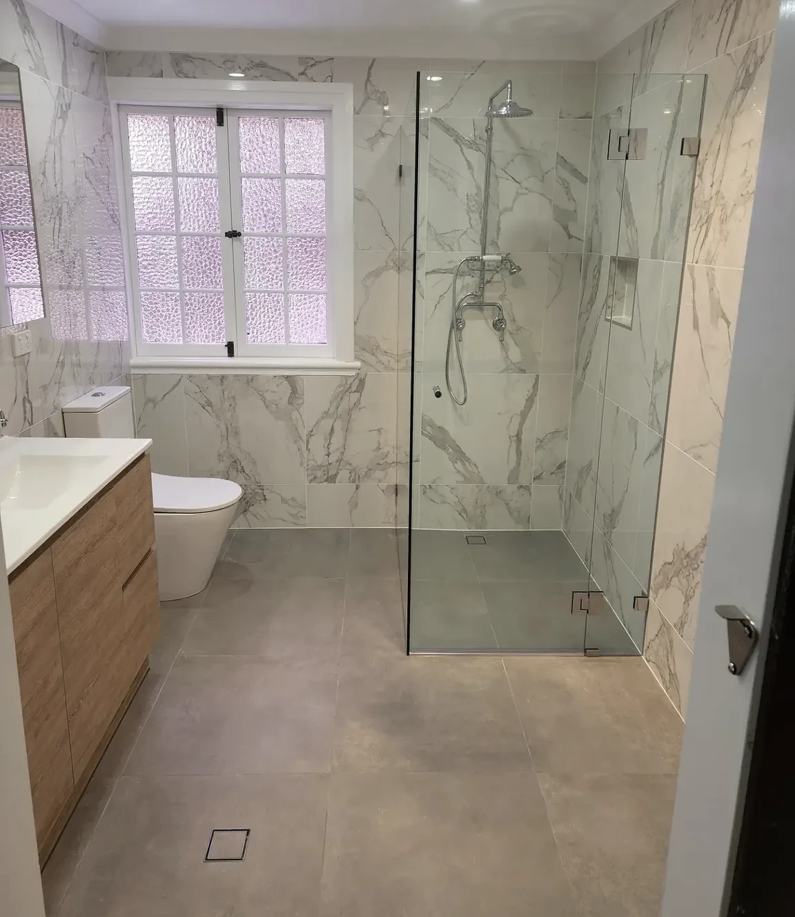 Bardon bathroom completed by O’D Tiling, with marble-look walls, a glass shower and grey floor tiles