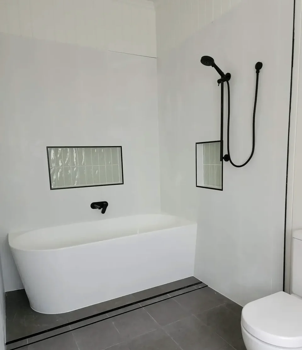 Paddington bathroom with a freestanding bath, black fittings and green tiled niches