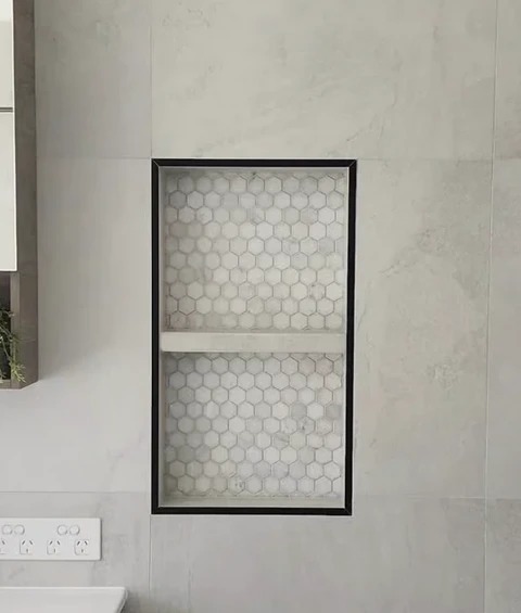 Close view of a mosaic-lined niche with a fitted shelf and dark trim